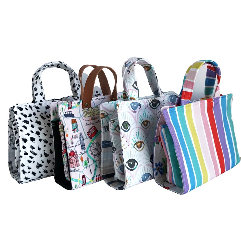 May include: Five different tote bags with various patterns. The bags are all made of a white fabric with different colored designs. The designs include a black and white polka dot pattern, a map of London, a pattern of eyes, and a rainbow striped pattern.