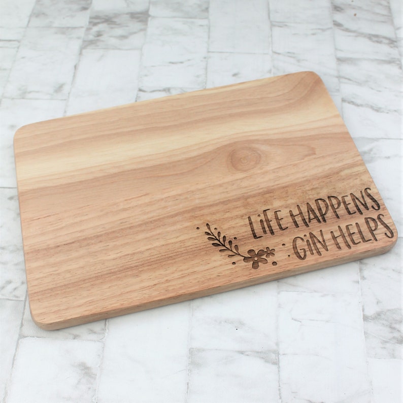 May include: A wooden cutting board with the text "Life Happens Gin Helps" engraved on it. The text is surrounded by a floral design.