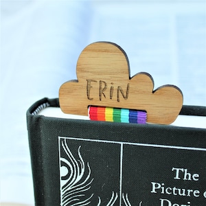 May include: Wooden cloud-shaped bookmark with the name "Erin" engraved on it. The bookmark has a rainbow ribbon attached to it.