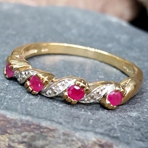May include: A gold ring with five round, bright red gemstones. The ring has a twisted design with small, clear accent stones. The band is a warm gold color, and the gemstones are set in a decorative pattern.
