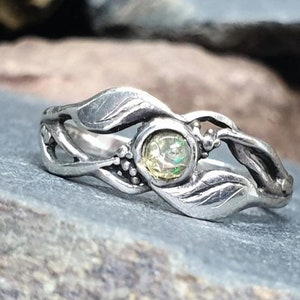 Könnte beinhalten: Ein silberner Ring mit einem zarten, blattförmigen Design und einem runden, schillernden Edelstein in der Mitte.