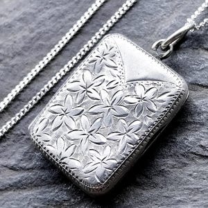 Op de afbeelding: Een zilveren rechthoekige hanger met een bloemmotief en bijpassende ketting. De hanger heeft een reliëf bloemenontwerp. De ketting is een delicate gourmette. De hanger is ongeveer 3 cm lang.