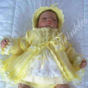 Puede incluir: Un vestido de bebé de punto amarillo con ribete de encaje blanco y un gorro a juego. El vestido tiene cierre de botón y un lazo de cinta en la cintura. El bebé lleva calcetines blancos y zapatos amarillos.