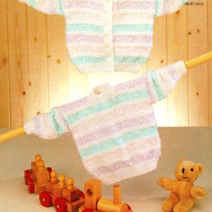 May include: Two pastel-striped knitted sweaters, one button-up cardigan and one pullover, are displayed. The text "DOUBLE KNITTING" is visible. The sweaters are hanging on wooden rods. A wooden toy train and a small teddy bear are in the foreground.