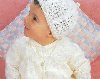 May include: A knitted baby outfit in cream color, including a bonnet, cardigan, and leggings. The bonnet has a cable knit design, and the cardigan has button closures. The leggings have a delicate lace pattern.
