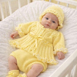 May include: A pale yellow knitted baby outfit consisting of a long-sleeved cardigan with a ribbon tie, matching bloomers, a bonnet with a ruffled edge, and booties with ribbon bows. The set features a textured knit pattern and delicate white trim.