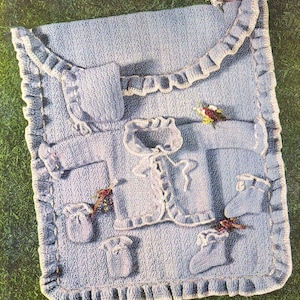 Op de afbeelding: Een gehaakte babydekenset in lichtblauw. De set bevat een deken, een jasje, een muts en slofjes. De deken heeft een gerimpelde rand.