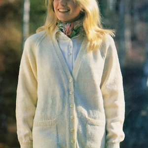 May include: A white knitted cardigan with a v-neck, long sleeves, and button closure. The cardigan has two pockets on the front and a ribbed hem and cuffs.