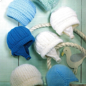 May include: Seven knitted baby hats in various colours, including white, blue, and green. The hats are displayed on a light blue wooden background with a rope and a seagull figurine.