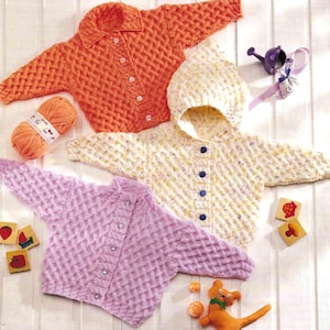 May include: Three hand-knitted baby sweaters in orange, yellow, and pink, each with a textured pattern and button closures. A ball of orange yarn and wooden blocks with fruit designs are also present.
