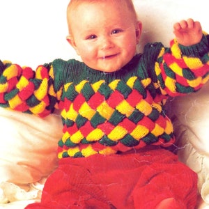 Puede incluir: Un bebé con un suéter tejido con un patrón de rombos de colores en rojo, amarillo y verde. El suéter tiene mangas largas y cuello redondo.