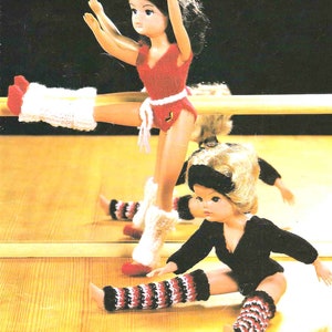 May include: Two dolls wearing knit leg warmers. One doll is wearing a red leotard and white leg warmers. The other doll is wearing a black leotard and red and white striped leg warmers.