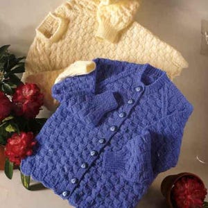 Könnte beinhalten: Zwei Strickjacken. Eine ist hellgelb, die andere ist eine blaue Strickjacke mit Knöpfen. Beide haben ein strukturiertes Muster. Die blaue Strickjacke hat eine Tasche. Die Strickjacken werden auf einer hellen Oberfläche präsentiert.