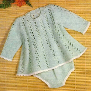 May include: A light green knitted baby outfit, featuring a long-sleeved top and matching diaper cover. The outfit has a delicate openwork design and white trim. The top has small buttons at the shoulder.