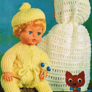 May include: A yellow knitted doll outfit with a matching hat and a white crocheted hooded cape. The doll is holding a blue and white rattle.