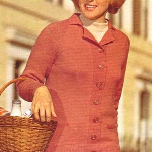 Könnte beinhalten: Ein korallenfarbener Cardigan mit Kragen und Knopfleiste. Die Frau hält einen Weidenkorb mit einer Flasche und anderen Gegenständen. Sie trägt einen gemusterten Rock und einen Rollkragenpullover.
