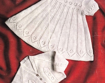 May include: A white knitted baby dress and matching cardigan set. The dress features a round neckline, short sleeves, and a flared skirt with diamond-shaped details. The cardigan has a button-up front and similar diamond patterns.