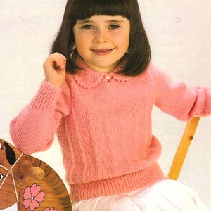 May include: A pink knitted sweater with a white crocheted collar and a pearl button. The sweater has a ribbed texture and long sleeves.