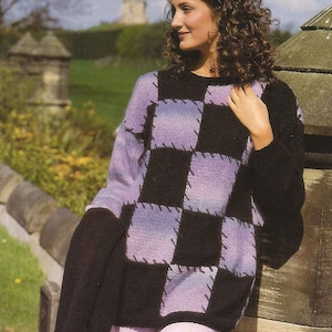 Op de afbeelding: Een vrouw draagt een zwart-paarse geruite trui met lange mouwen en een losse pasvorm. Ze staat voor een stenen muur en groen gras.