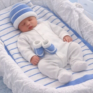 May include: A white long-sleeved onesie, a blue and white striped knit hat, and a pair of matching blue and white knit booties. The items are displayed on a white and blue striped fabric liner with a white lace trim border.