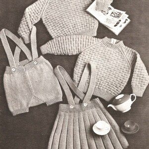 May include: A knitted baby outfit set in a light beige color. The set includes a sweater, a skirt with suspenders, and a pair of shorts with suspenders.