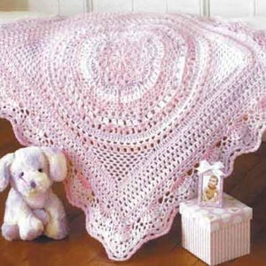 May include: A pink and white crocheted baby blanket with a scalloped edge. The blanket is made with a delicate stitch pattern and has a circular design in the centre.