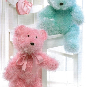 May include: Two knitted teddy bears, one pink and one light blue, sitting on a white chair. The pink bear has a pink ribbon around its neck.