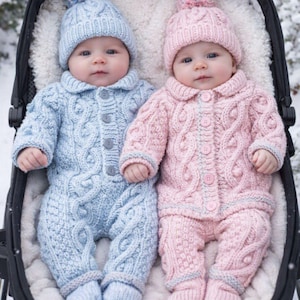 May include: Two infants wearing matching cable-knit outfits in light blue and soft pink. Each outfit includes a long-sleeved button-up romper with integrated booties and a matching beanie topped with a multi-coloured pom-pom, resting in a stroller.