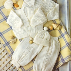 May include: A white knitted baby outfit set with a cardigan, trousers, and a hat. The set is made with a delicate openwork stitch pattern.