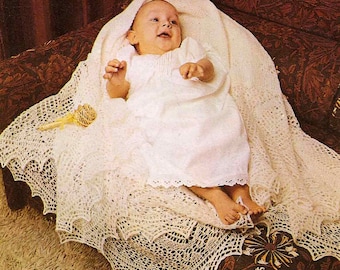 May include: A white crocheted baby blanket with a delicate lace pattern. A baby is lying on the blanket, wearing a white gown.