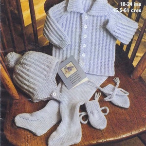 Könnte beinhalten: Ein gestricktes Baby-Set in helllila, bestehend aus einer Strickjacke, einer Mütze, Stiefeln und Leggings. Die Strickjacke hat einen Knopfleisten vorne und eine gerippte Struktur. Das Set liegt auf einem Holzstuhl.