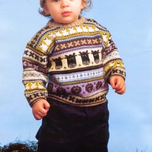 May include: A child in a knitted sweater and hat set. The sweater displays a pattern of sheep, bears, and geometric shapes in brown, green, purple, and white. The child is also wearing dark blue trousers.