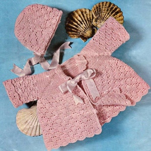 May include: A pink crocheted baby jacket and matching hat. The jacket has a scalloped edge and a bow at the neckline. The hat is a simple beanie style.