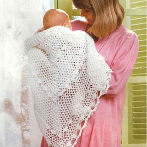 Op de afbeelding: Een vrouw in een roze jurk houdt een baby vast die gewikkeld is in een wit gehaakt dekentje. Het dekentje heeft een delicaat kantpatroon en is perfect voor een pasgeboren baby.