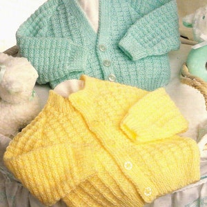 May include: Two knitted baby cardigans, one in light blue and one in yellow. Both cardigans have a button fastening and a ribbed texture.