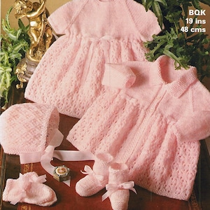 May include: A pink knitted baby dress, cardigan, hat and booties. The dress and cardigan have a lacy pattern. The hat has a bow. The booties have bows. The text on the image reads "BQK 19 ins 48 cms".