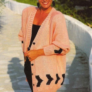 Puede incluir: Un cárdigan de punto rosa con diseños de flechas negras en la parte delantera y botones negros. El cárdigan tiene mangas largas y cuello en V.