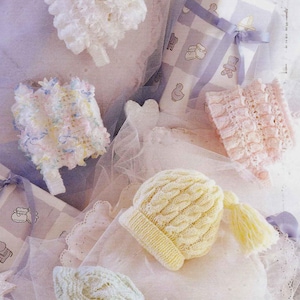 May include: An assortment of baby bonnets and a cable-knit hat in soft pastel colors. The image includes a white bonnet with a ruffled edge, a pink bonnet, and a yellow hat with a tassel. A gift box with a blue ribbon is also present.