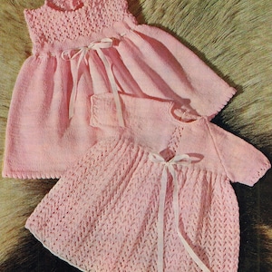 Pode incluir: Dois vestidos de bebé de malha rosa com laços brancos. O vestido de cima tem um corpete texturizado e uma saia simples. O vestido de baixo tem um padrão de renda em todo.