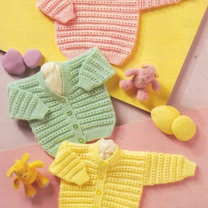 May include: Three knitted baby sweaters in pink, green and yellow with button fastenings. The sweaters are laid out on a pink and yellow surface with small stuffed toys.