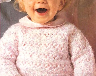 以下が含まれることがあります： 白いレース模様のピンクのニットセーターを着た小さな女の子。彼女は笑顔で、ブロンドの髪をしています。