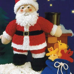May include: A knitted Santa Claus doll wearing a red suit with white trim and a white beard. He is holding a blue bag with a white drawstring and is standing on a snowy surface. There are other knitted toys in the background.