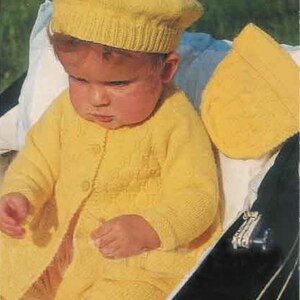 May include: A baby wearing a yellow knitted outfit, including a beret with a pom-pom, a cardigan, and pants. The outfit is buttoned up and appears to be handmade. The image also shows a matching knitted hat. The number "8143" is in the top right corner.