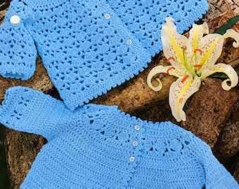 May include: Two light blue crocheted cardigans featuring long sleeves and small white buttons. The top cardigan has a textured open-stitch pattern, while the bottom cardigan displays a solid stitch body with decorative open-work detailing at the yoke.