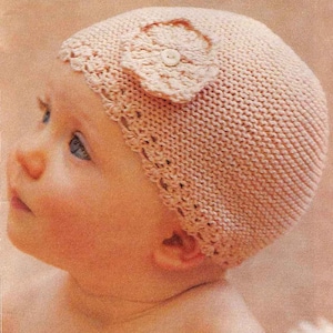 May include: A pink knitted baby hat with a crocheted flower detail and a white button in the center.