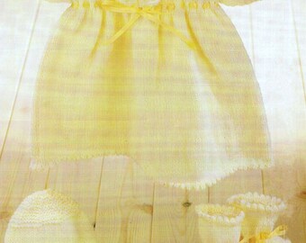 May include: A knitted baby outfit in a pale yellow color. The set includes a dress with a crocheted collar and a matching hat and booties.