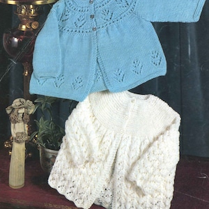 Könnte beinhalten: Zwei gestrickte Baby-Cardigans, einer in hellblau und einer in weiß, mit Knopfleiste und Spitzendetails.