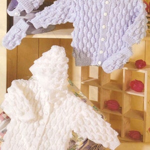 Pode incluir: Dois cardigans de malha para bebé com ponto de bolinha texturizado. Um cardigan é branco e o outro é roxo claro. Ambos os cardigans têm fecho de botão. Há também dois chapéus de malha e dois pares de luvas de malha.