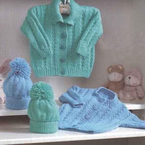 May include: A selection of knitted baby clothes in shades of blue and green. The items include a button-down cardigan, a hat with a pom-pom, and a sweater. The cardigan is hanging on a wooden hanger. Two teddy bears are in the background.