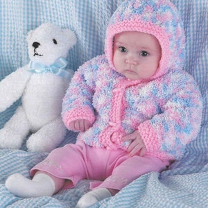 Może przedstawiać: Dziecko w różowej i niebieskiej dzianinowej kurtce z kapturem, obok którego siedzi biały miś.